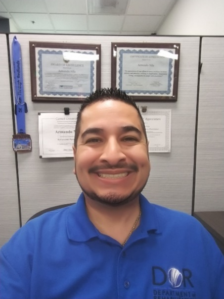 Smiling man wearing blue DOR polo sitting in a cubicle