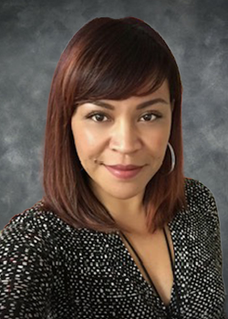 Woman with shoulder length reddish-brown hair wearing silver hoop earrings and a black and white spotted blouse