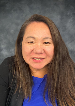 Woman with long brown hair wearing a black blazer over a blue blouse