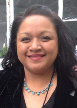 Woman with black hair wearing a black jacket over a black shirt and teal necklace