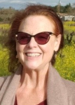 Woman with brown hair wearing brown sunglasses standing in a field