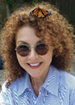 Woman with curly brown hair with a monarch butterfly sitting near her forehead wearing a blue collard shirt