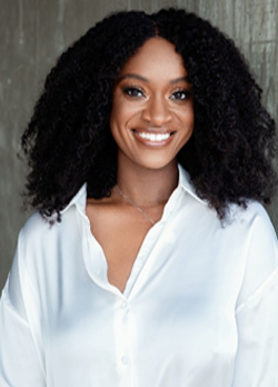 Woman with curly, black, shoulder length hair wearing a white, button up blouse
