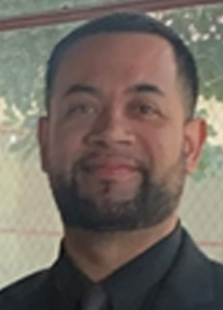 Man with short black hair and close trimmed beard wearing a black shirt with black tie
